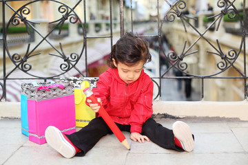 Little cute boy sits on floor near wrought railings and draws