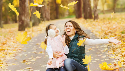 Mother and daughter having fun in the autumn park among the fall