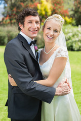 Attractive bride and groom smiling at camera and hugging
