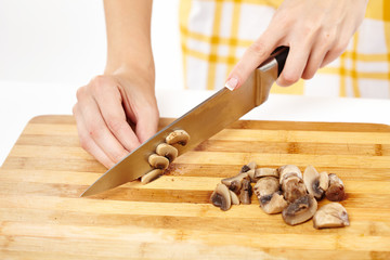 Woman cook's hands chopping mushrooms on a wooden board