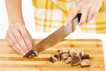 Obraz na płótnie Canvas Woman cook's hands chopping mushrooms on a wooden board