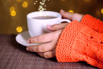 Hands holding mug of hot drink, close-up, on bright background