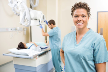 Nurse Smiling While Colleague Preparing Patient For Xray - obrazy, fototapety, plakaty