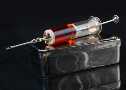 Glass syringe with stainless steel box on a black background.