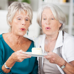 zwei ältere freundinnen blasen kerzen auf dem kuchen aus