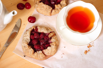 Cherry tart with tea on wooden table with knife and teapot