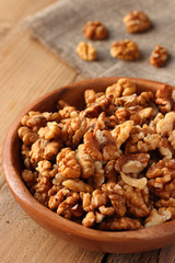Shelled walnuts in wooden bowl on wooden background