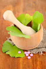Ginkgo biloba leaves in mortar and pills on wooden background