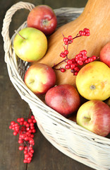 Juicy apples and pumpkin in wooden basket on table close-up