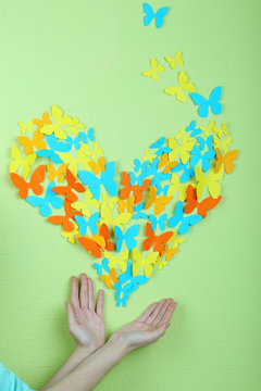 Paper butterflies on hands on green wall background