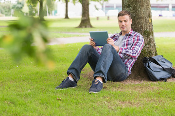 Obraz premium Happy student using his tablet pc outside leaning on tree