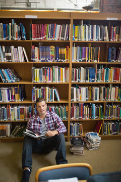 Happy young student sitting on library floor reading