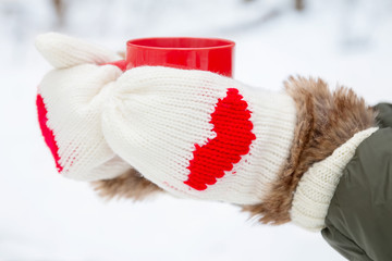 Hands in mittens with hearts holding cup