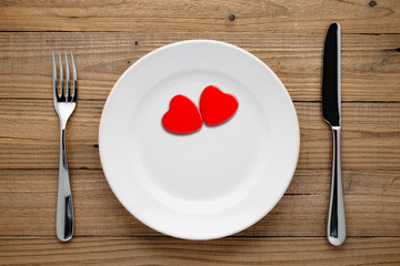 Fototapeta na wymiar Two red hearts on plate on wooden background