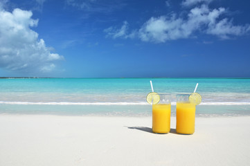 Two glasses of orange juice on the sandy beach