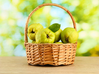 sweet quinces with leaves in basket, on green background