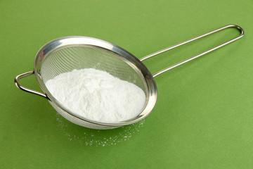 Powdered sugar in metal sieve on green background