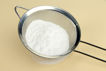 Powdered sugar in metal sieve on beige background