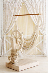 Beautiful wooden ship wheel in room decorated with curtains.
