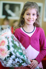 Happy beautiful girl with bunch of white flowers stands in class