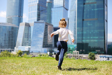 Back of little girl running on grass near skyskrapers