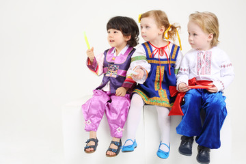 Little boys and girl in folk costumes sits with sticks on white