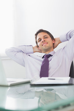 Relaxed businessman with hands behind head in office