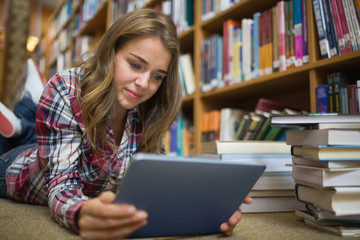 Young pretty student lying on library floor using tablet