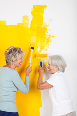 zwei lachende seniorinnen streichen die wohnung