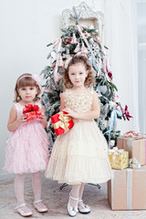 Two little girls with gifts near a Christmas fir-tree