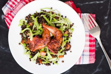 Delicious salad with black lentils, fried legs quail, tomatoes