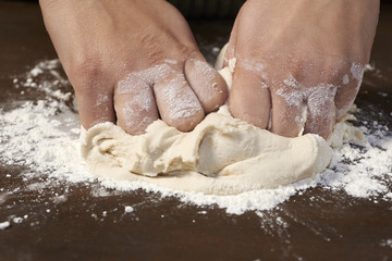 woman's hands kneading dough on wooden table