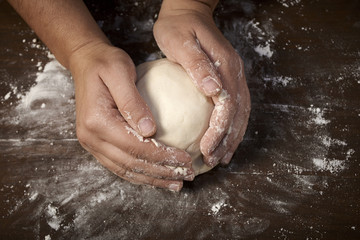 woman's hands kneading dough on wooden table - obrazy, fototapety, plakaty