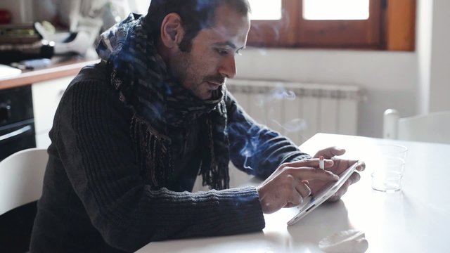 young man using tablet and smoking at home on the table