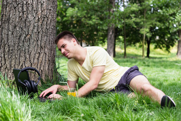Naklejka na ściany i meble Cheerful young male using laptop in the park