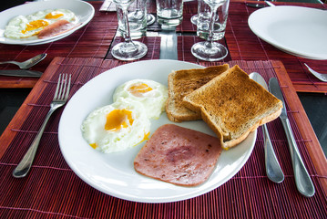Bacon, fried eggs and toast on white plate