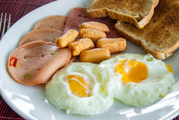Bacon, fried eggs, sausage and toast on white plate