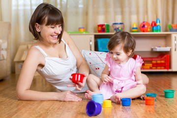 Obraz na płótnie Canvas kid girl and mother playing together with cup toys
