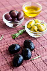 Plates of green olives, black olives and olive oil on bamboo nap