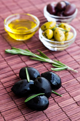 Plates of green olives, black olives and olive oil on bamboo nap