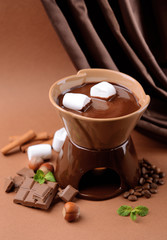 Chocolate fondue with marshmallow candies, on brown background