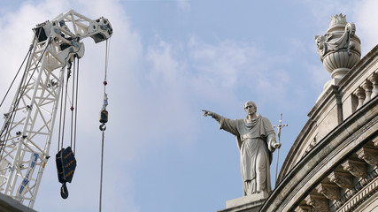 Fototapeta na wymiar Christian statue on building pointing towards construction crane