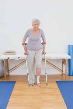 Senior woman with crutches in the hospital gym