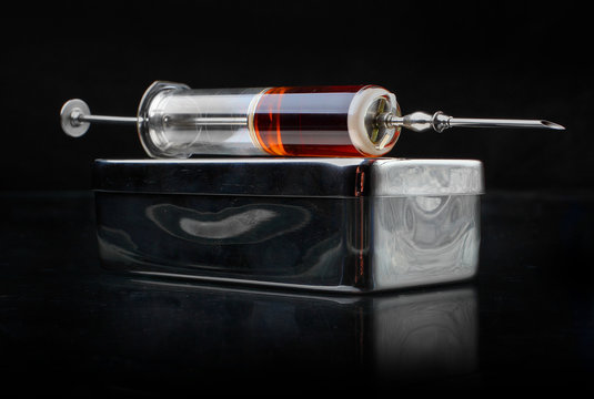 Glasss syringe with stainless steel box on a black background.