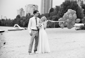 happy bride holding balloons on beach and hugging groom