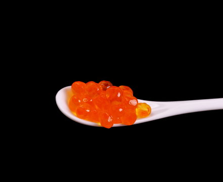 Porcelain spoon full of red salmon caviar on black background