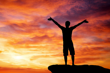 Fototapeta premium Silhouette of a man on a mountain top on fiery orange background