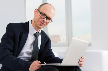 Young smiling businessman sitting on couch with laptop
