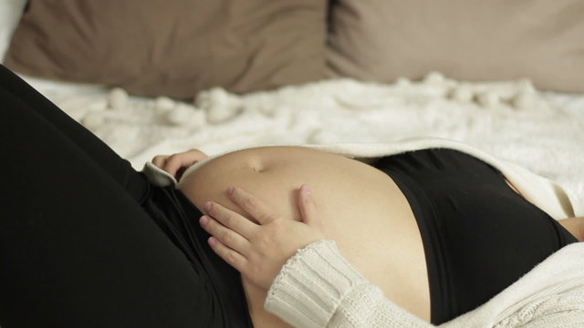 Pregnant woman touches her belly, close up