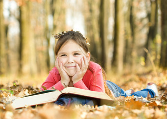 Little girl is reading a book outdoors